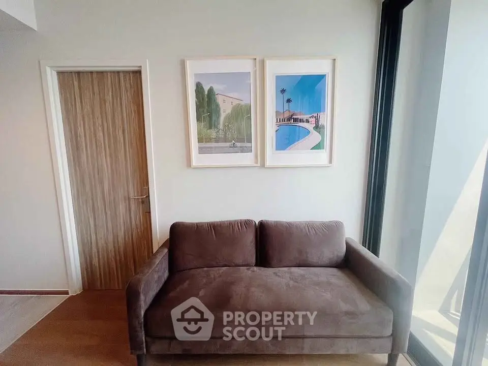 Modern living room with stylish brown sofa and framed art, featuring large windows for natural light.