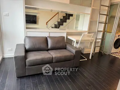 Modern living room with sleek black sofa and stylish workspace, featuring a contemporary staircase and wooden flooring.