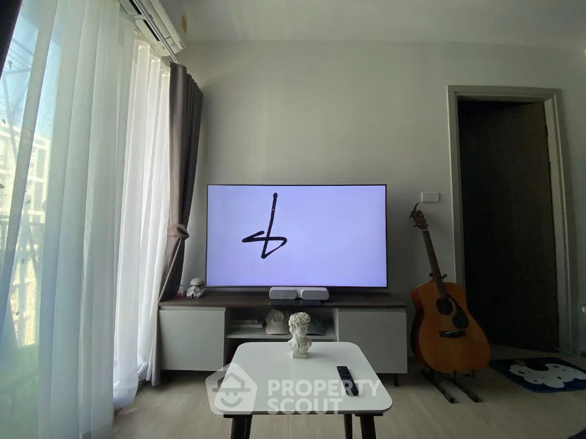 Modern living room with TV, guitar, and natural light from large window.