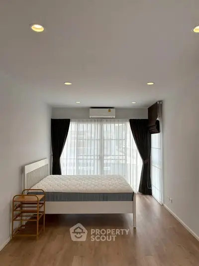 Spacious bedroom with large windows and wooden flooring, featuring a modern bed and elegant curtains.