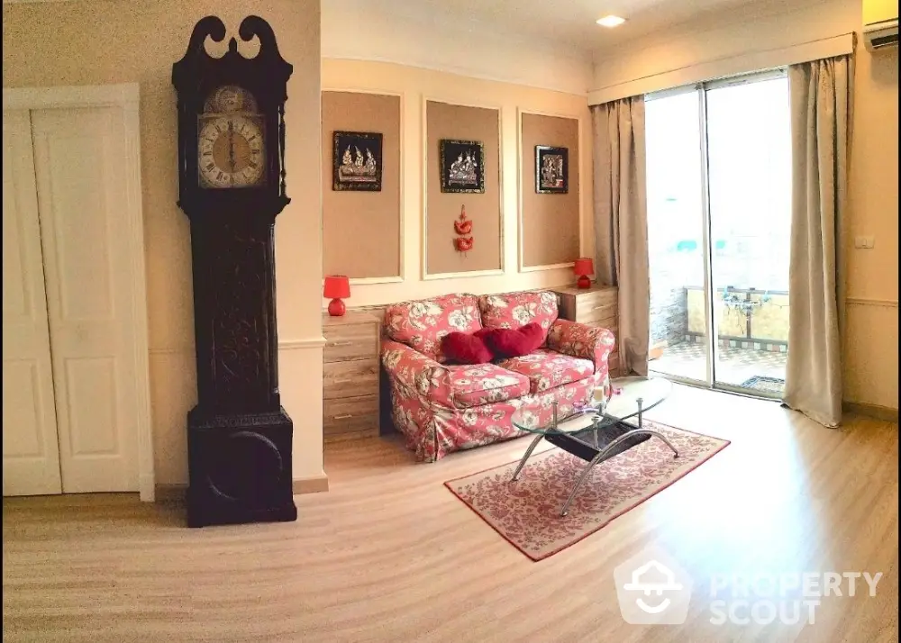 Charming living room with floral sofa and antique clock, featuring large windows and elegant decor.