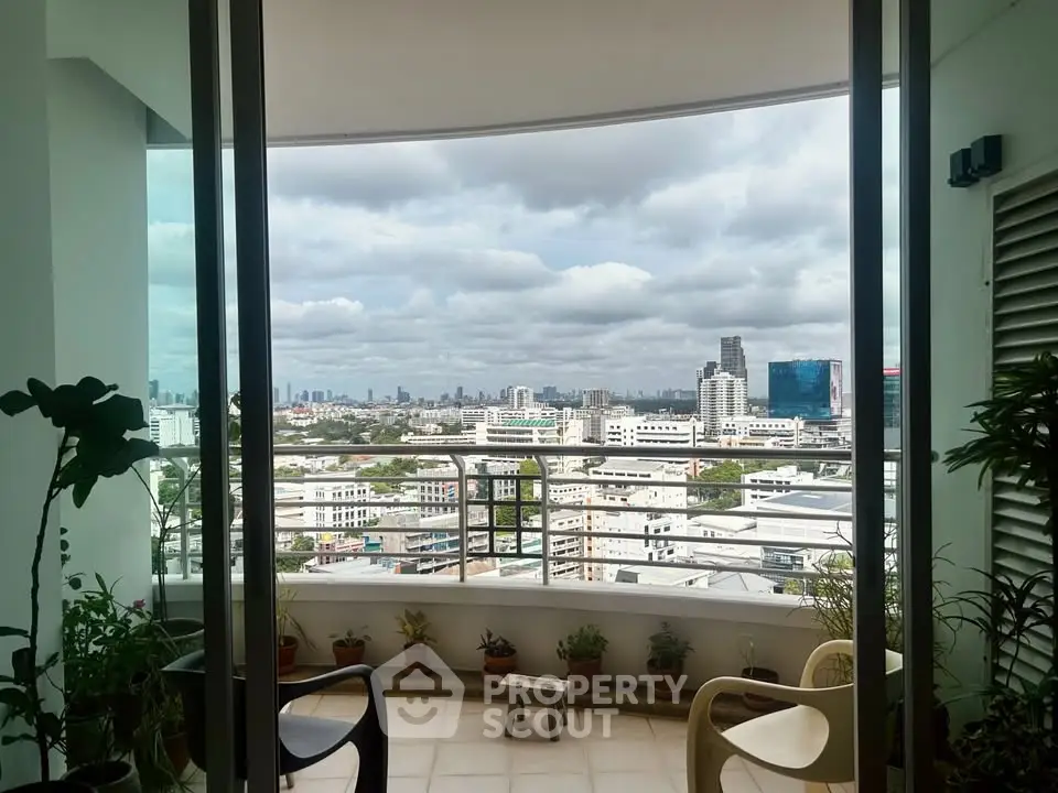 Stunning cityscape view from a high-rise balcony with lush potted plants and cozy seating.