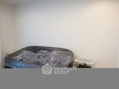 Minimalist bedroom with a bed covered in plastic wrap, showcasing a clean and simple design.