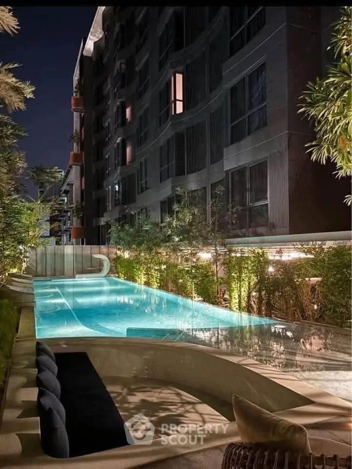 Luxurious apartment building with illuminated pool and lush greenery at night, perfect for upscale living.