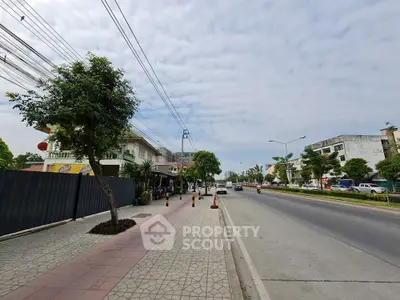 Spacious urban street view with sidewalk and trees, ideal for commercial real estate opportunities.