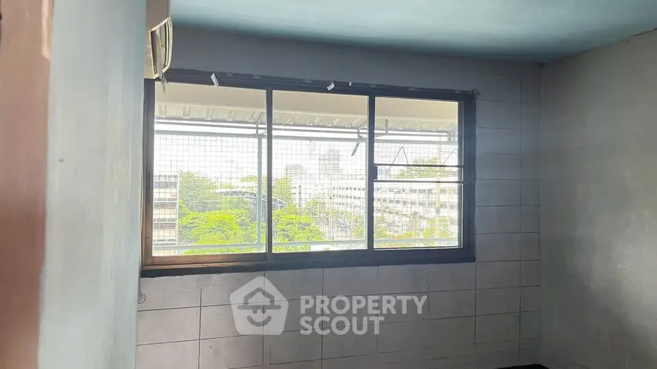 Spacious room with large window offering city view and natural light.