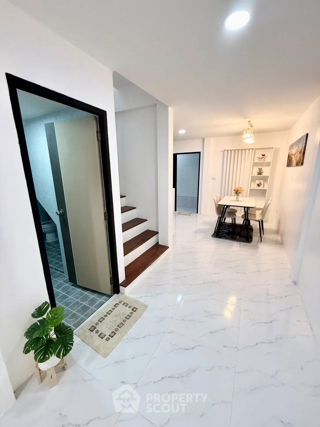 Modern interior with sleek dining area and staircase, featuring elegant white flooring.