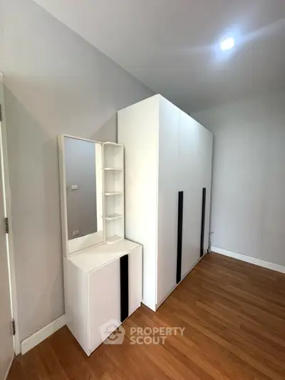 Spacious bedroom with modern wardrobe and vanity set on wooden flooring.