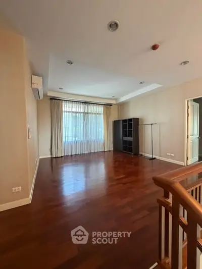 Spacious empty living room with hardwood floors and large window in modern home.