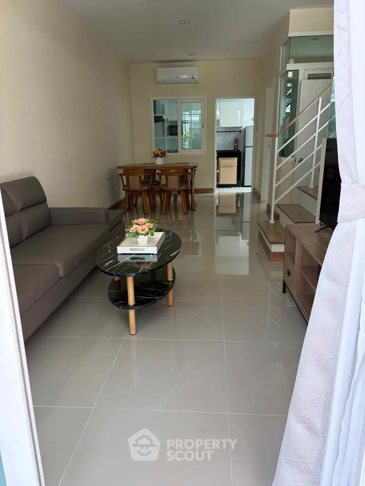 Spacious living room with modern furniture and open layout leading to dining area and kitchen.