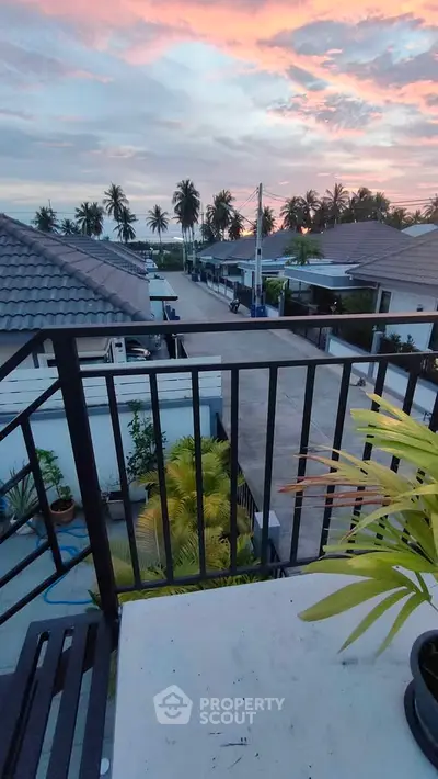 Charming balcony view with tropical sunset and palm trees in a serene neighborhood.