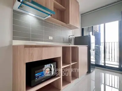 Modern kitchen with sleek cabinetry, microwave, and fridge in a bright apartment with balcony access.