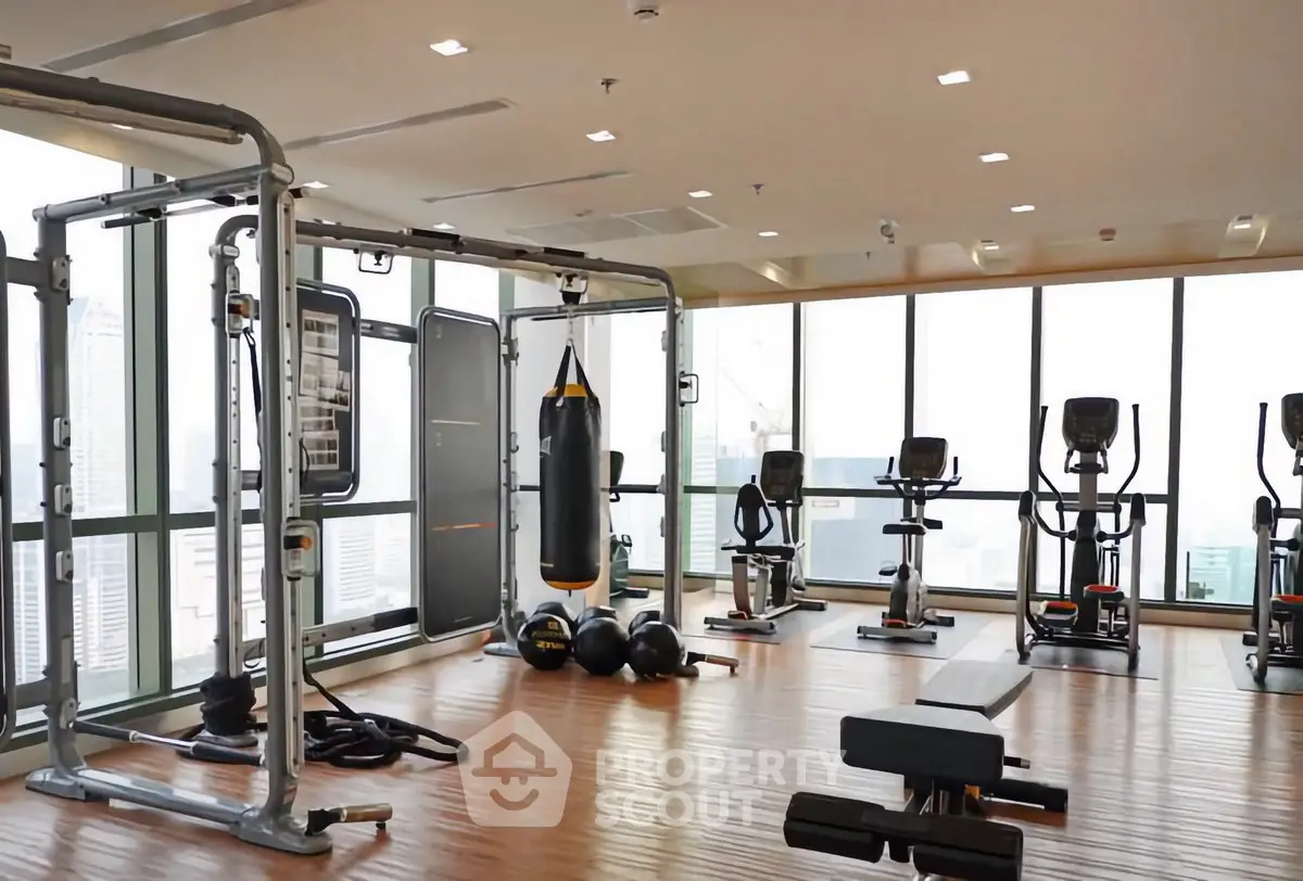 Spacious gym with modern equipment and city view in luxury apartment building.