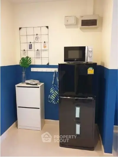 Compact kitchen corner with fridge, microwave, and storage in modern apartment.