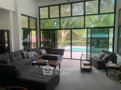Spacious living room with large windows overlooking a serene pool and lush greenery.