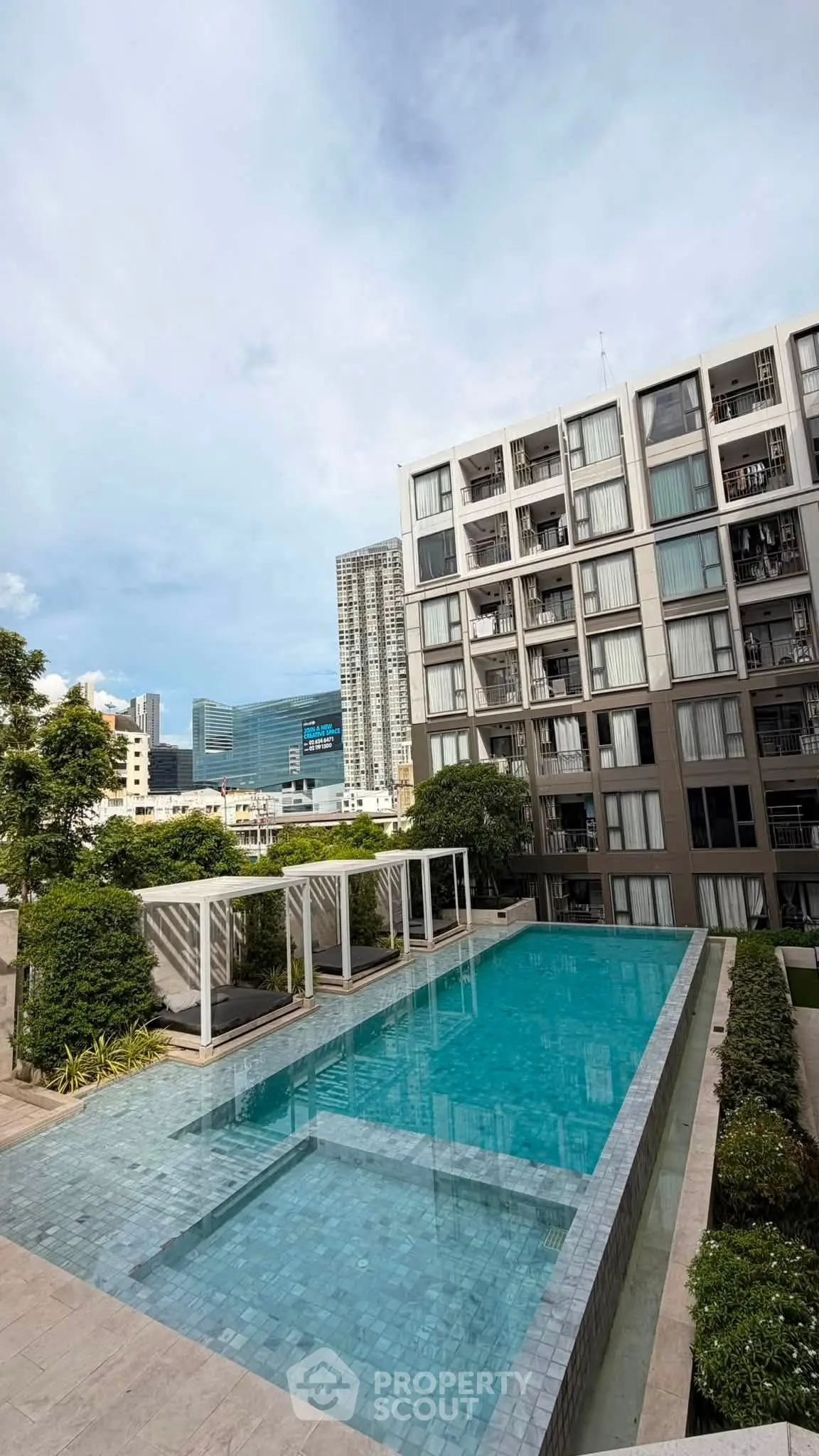 Modern apartment building with a luxurious outdoor pool and city skyline view.
