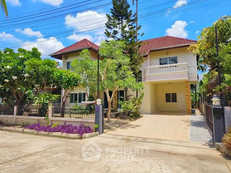 Charming two-story house with lush garden and spacious driveway under a bright blue sky.