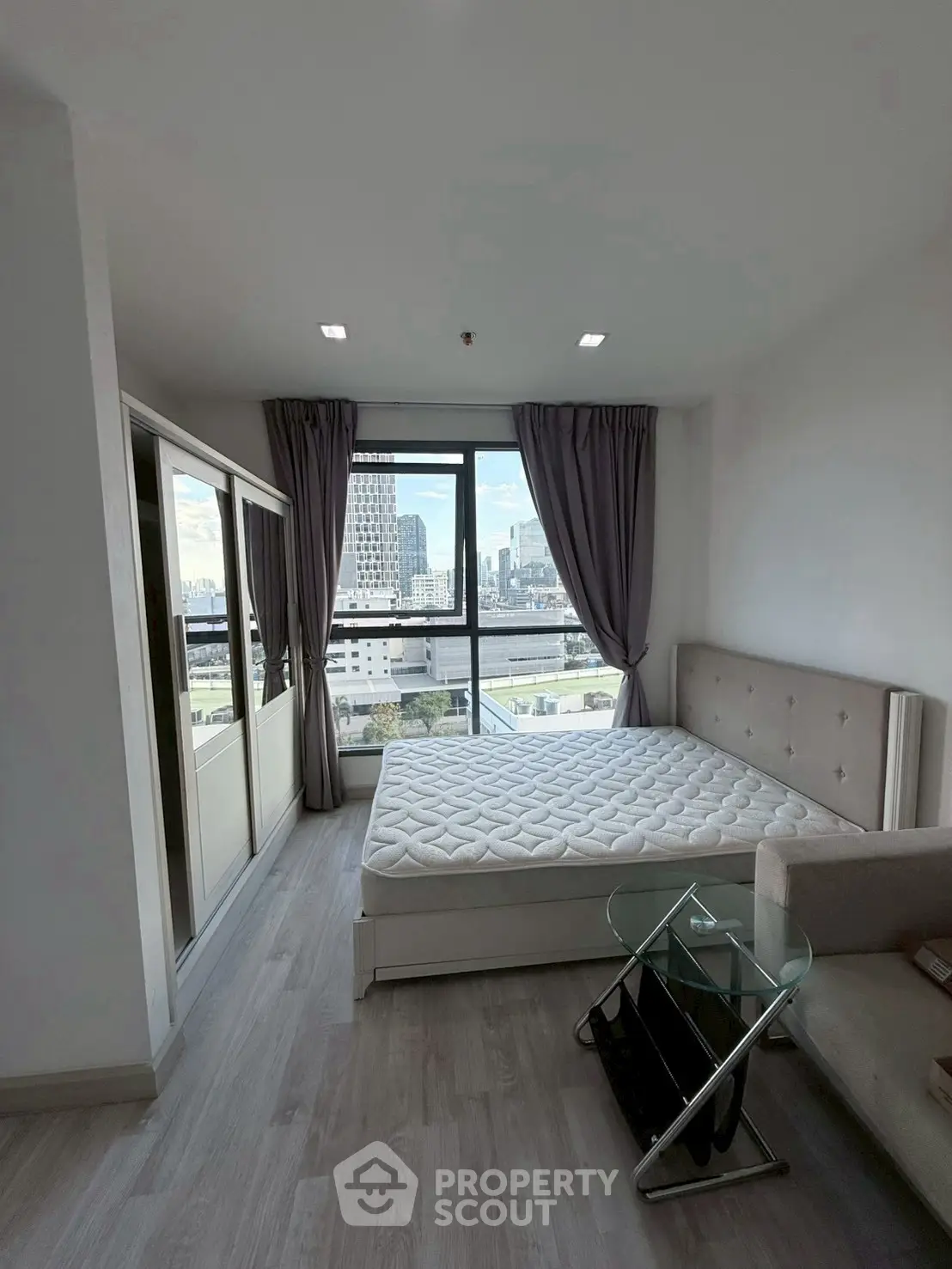 Modern bedroom with city view, featuring a stylish bed and glass side table, perfect for urban living.
