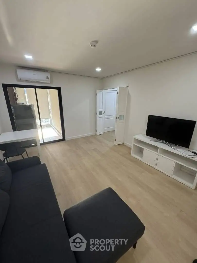 Modern living room with sleek furniture and natural light, featuring a TV and air conditioning.
