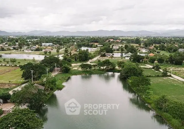 Scenic aerial view of lush green landscape with serene water body and distant mountains.