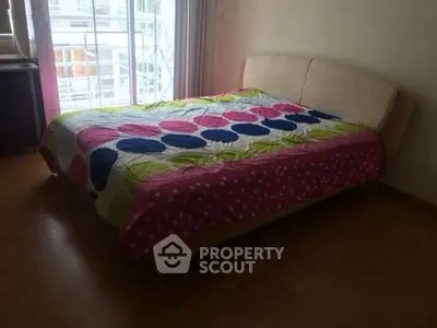 Cozy bedroom with colorful bedding and natural light from large window.