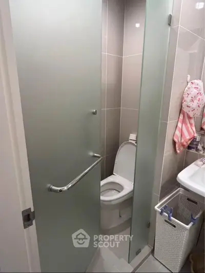 Compact modern bathroom with frosted glass door and sleek fixtures.