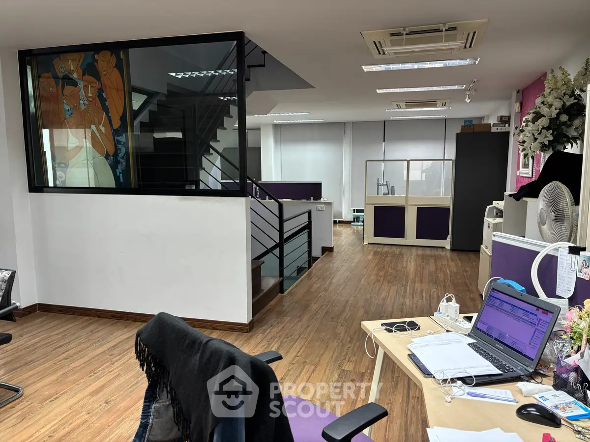 Modern office space with wooden flooring and open layout, featuring a staircase and contemporary decor.