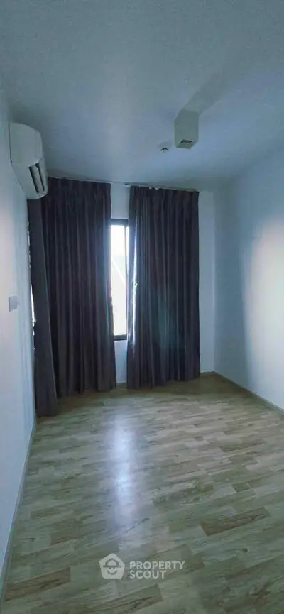 Spacious empty room with wooden flooring and large window, perfect for customization.