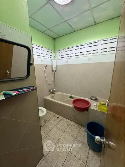 Cozy bathroom with bathtub and shower in a compact layout, featuring green walls and tiled flooring.