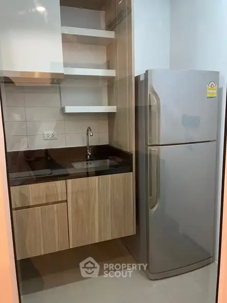 Modern compact kitchen with sleek cabinetry and stainless steel fridge