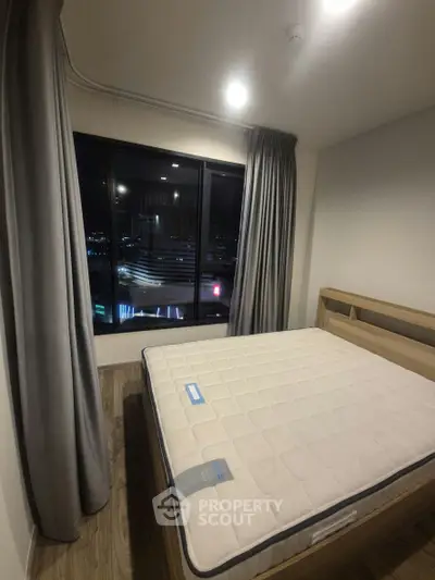 Cozy bedroom with large window offering stunning night city view, featuring a comfortable bed and elegant curtains.