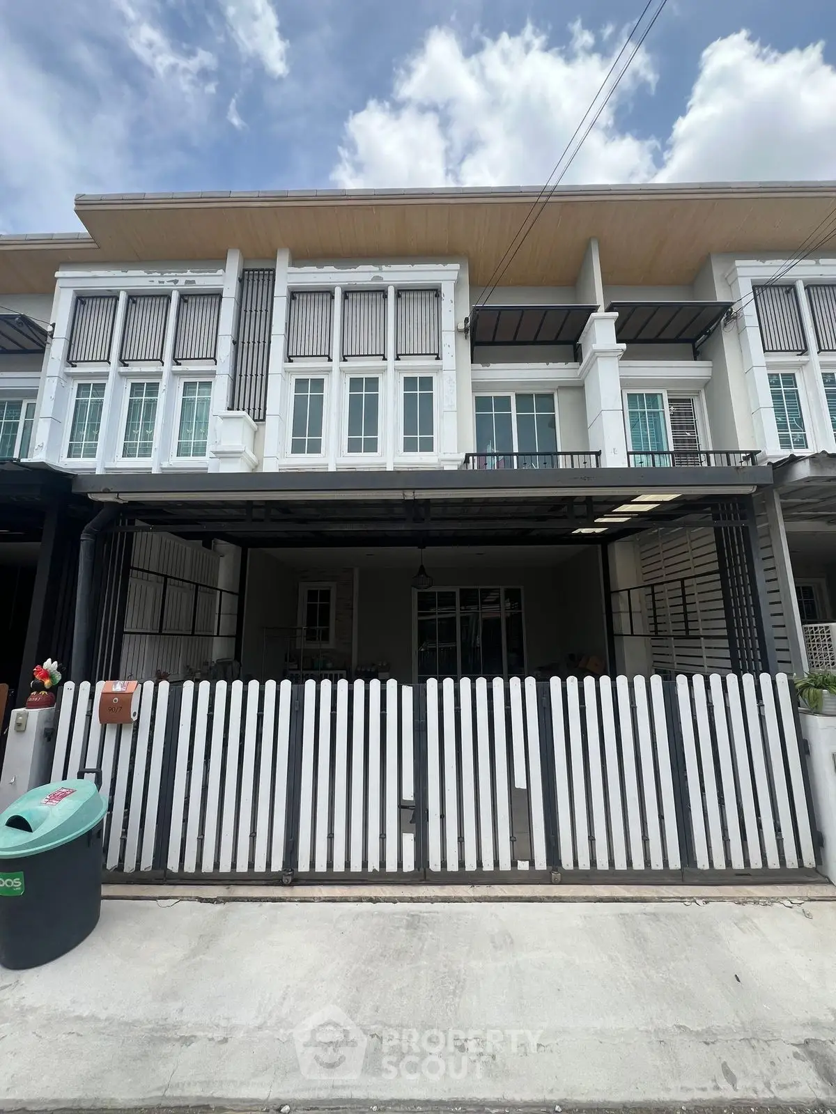 Modern townhouse exterior with white picket fence and large windows under a clear sky.