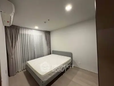 Spacious bedroom with modern design and natural light, featuring a comfortable bed and elegant curtains.