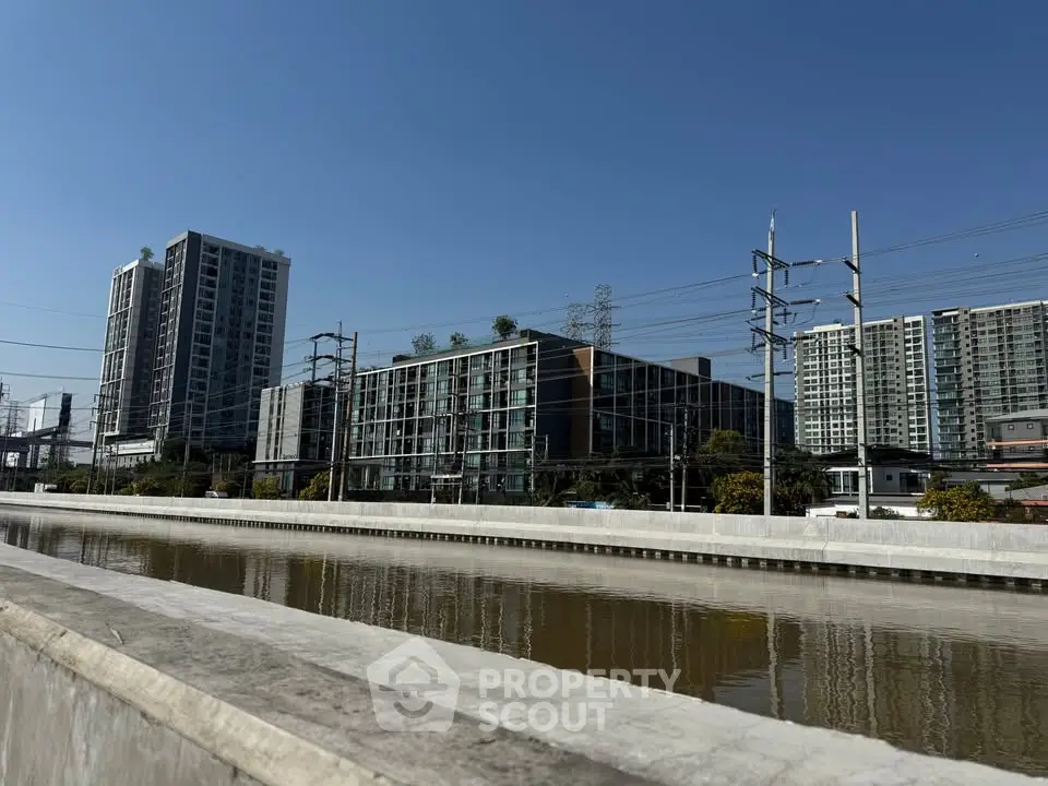 Modern apartment buildings with clear blue sky and canal view, ideal urban living.