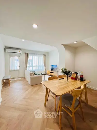 Modern living room with dining area and natural light, featuring wooden flooring and stylish furniture.
