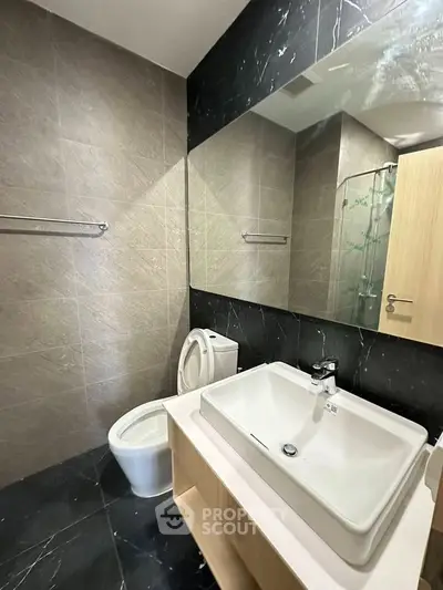 Modern bathroom with sleek design featuring a large mirror, stylish sink, and elegant tile work.