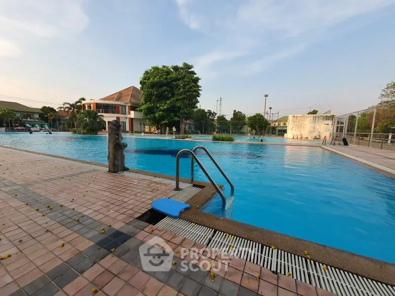 Spacious outdoor pool area with clear blue water and surrounding greenery, perfect for relaxation.