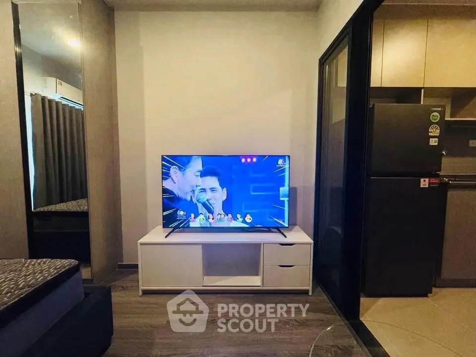 Modern studio apartment with sleek TV setup and compact kitchen area.