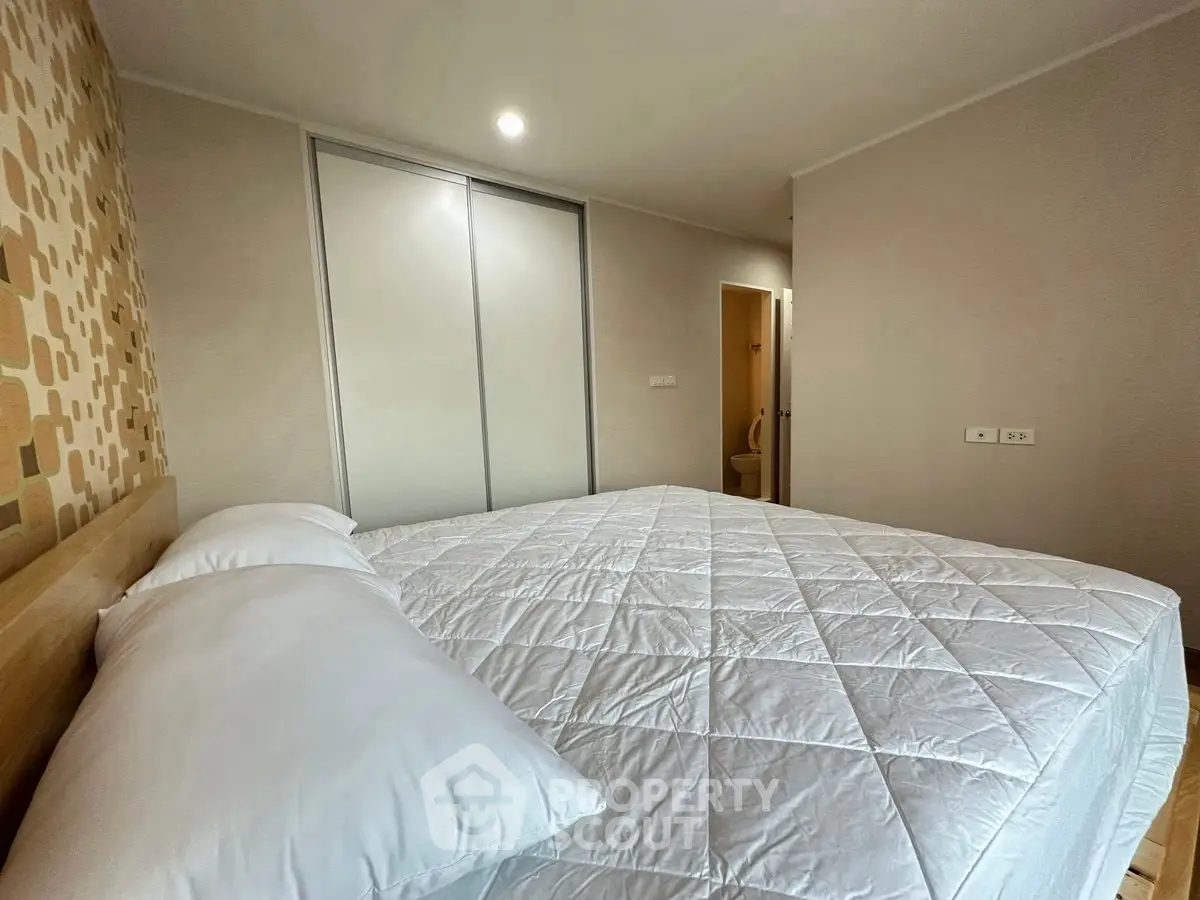 Spacious bedroom with modern decor and ample natural light, featuring a comfortable bed and stylish closet.