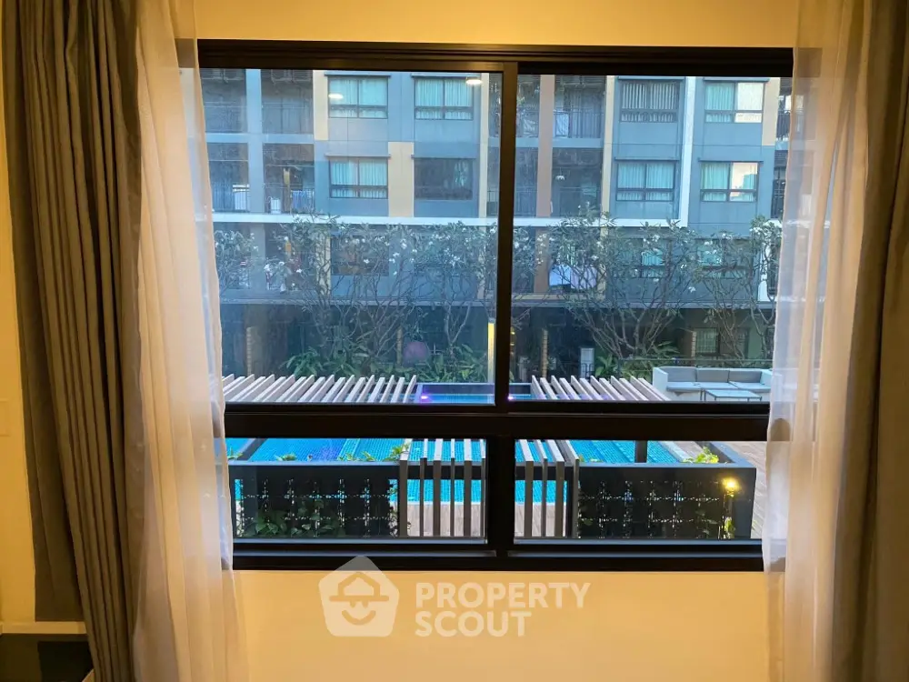 Luxurious apartment window view overlooking modern pool and garden area.