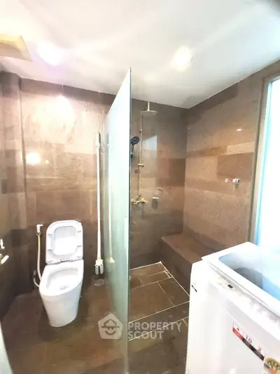 Modern bathroom with glass shower and washing machine in sleek design.