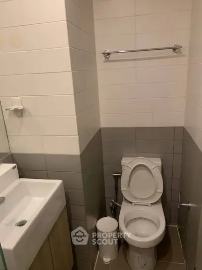 Modern bathroom with sleek design and neutral tiles, featuring a compact sink and toilet.