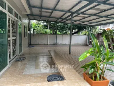 Spacious covered patio with tiled flooring and lush greenery, perfect for outdoor relaxation.