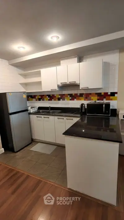 Modern kitchen with sleek cabinets, colorful backsplash, and stainless steel appliances.