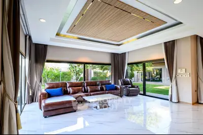 Luxurious living room with leather sofa and garden view, featuring modern ceiling design and large windows.