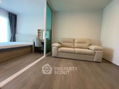 Modern apartment interior with cozy living room and bedroom separated by glass partition.