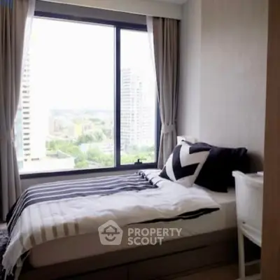 Cozy bedroom with large window offering stunning city view, perfect for urban living.