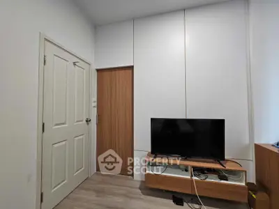 Modern minimalist living room with sleek white walls, wooden accents, and a flat-screen TV, perfect for cozy urban living.