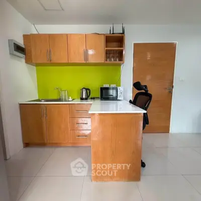 Modern kitchen with wooden cabinets, green backsplash, and sleek appliances in a compact layout.