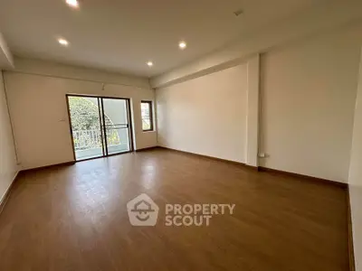 Spacious empty room with wooden flooring and balcony access, perfect for customization.